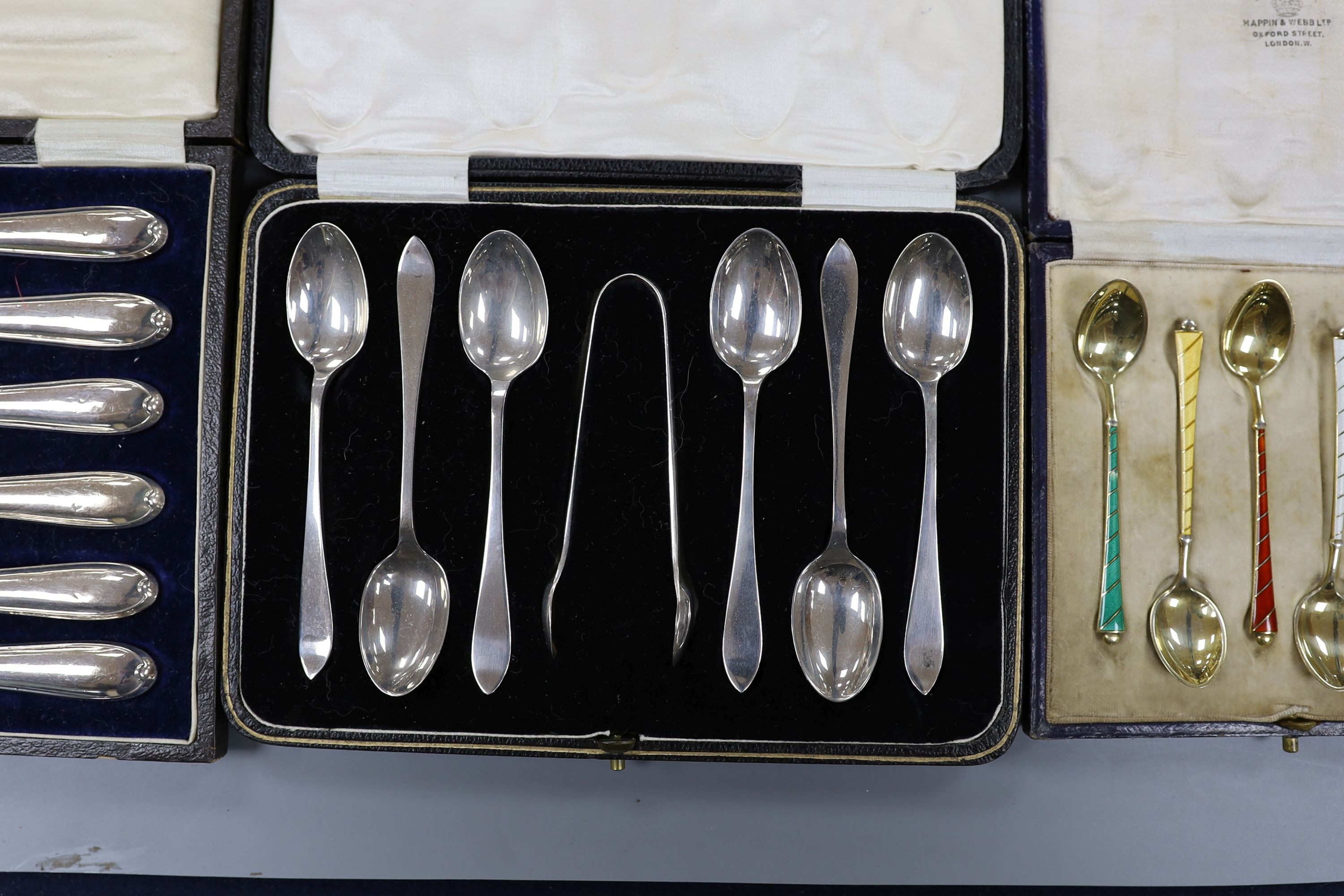 A cased set of six Danish gilt sterling and polychrome enamel coffee spoons, a cased set of six silver teaspoons with tongs and a cased set of six silver handled tea knives.